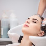 Revel in rest. Pleasant beautiful woman leaning on the sing while professional hairdresser washing her head